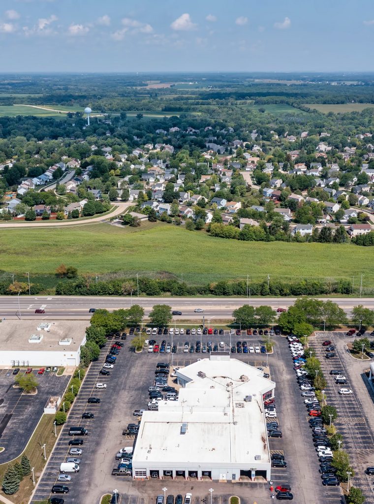 A aerial showing a parcel of land for sale near a housing development and retail shopping center in a suburban area.
